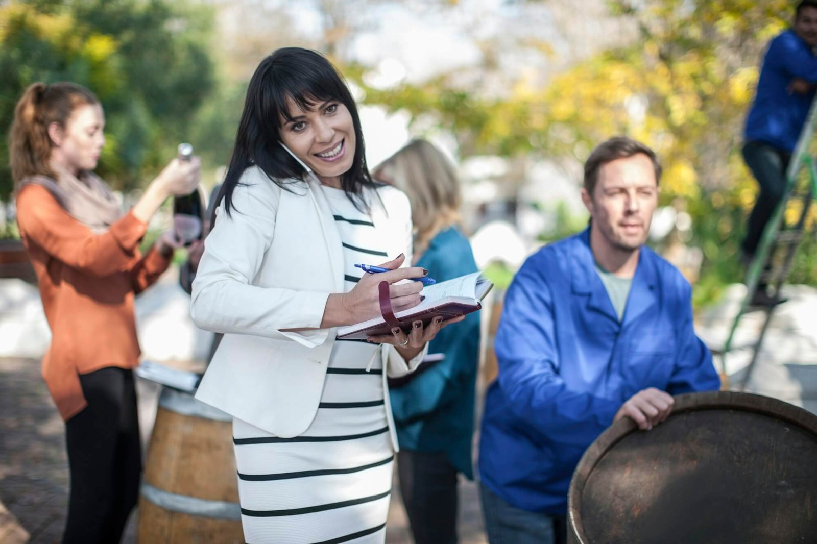 wine saleswoman with group of clients outdoors and wine worker with barrel